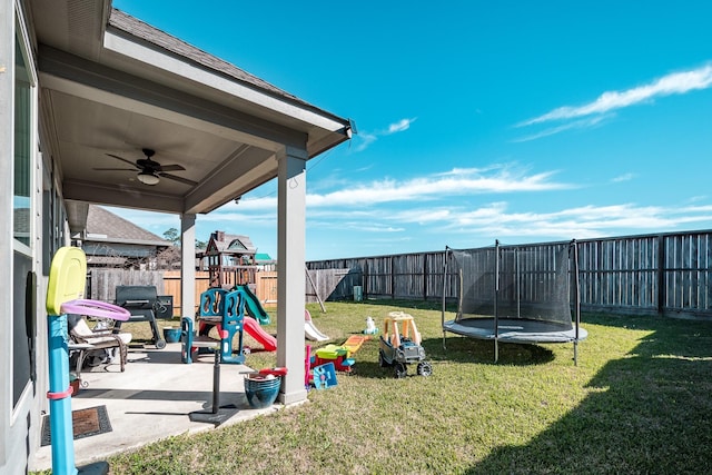 exterior space with a patio, a fenced backyard, a ceiling fan, a lawn, and a trampoline