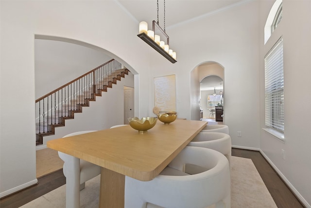 dining space featuring crown molding, baseboards, dark wood-type flooring, a towering ceiling, and arched walkways