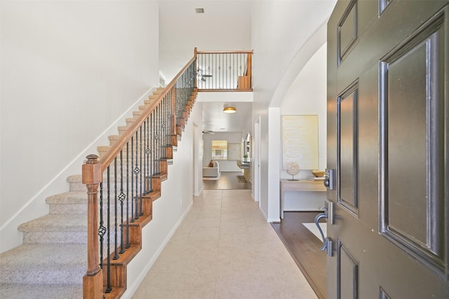 tiled foyer featuring baseboards, arched walkways, a high ceiling, and stairway