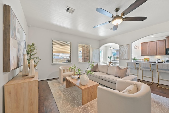 living area featuring ceiling fan, dark wood-style floors, visible vents, and arched walkways