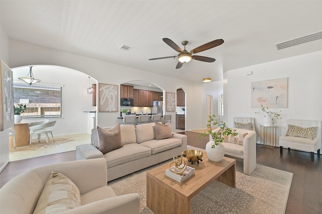 living area with arched walkways, visible vents, dark wood-style flooring, and ceiling fan