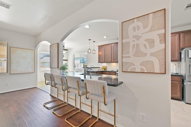 kitchen featuring tasteful backsplash, visible vents, a kitchen bar, freestanding refrigerator, and a sink