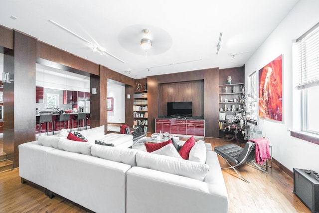 living area featuring built in features, a healthy amount of sunlight, track lighting, and wood finished floors