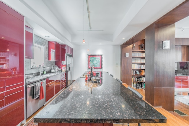 kitchen with tasteful backsplash, a spacious island, a tray ceiling, stainless steel appliances, and a sink