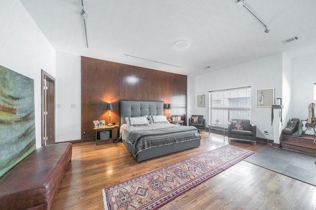 bedroom with wooden walls, track lighting, visible vents, and wood finished floors