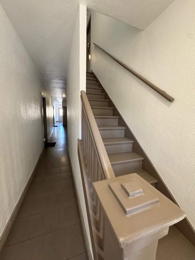 stairway featuring a textured ceiling, a textured wall, baseboards, and tile patterned floors