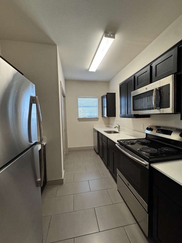 kitchen with light tile patterned floors, stainless steel appliances, dark cabinetry, light countertops, and a sink