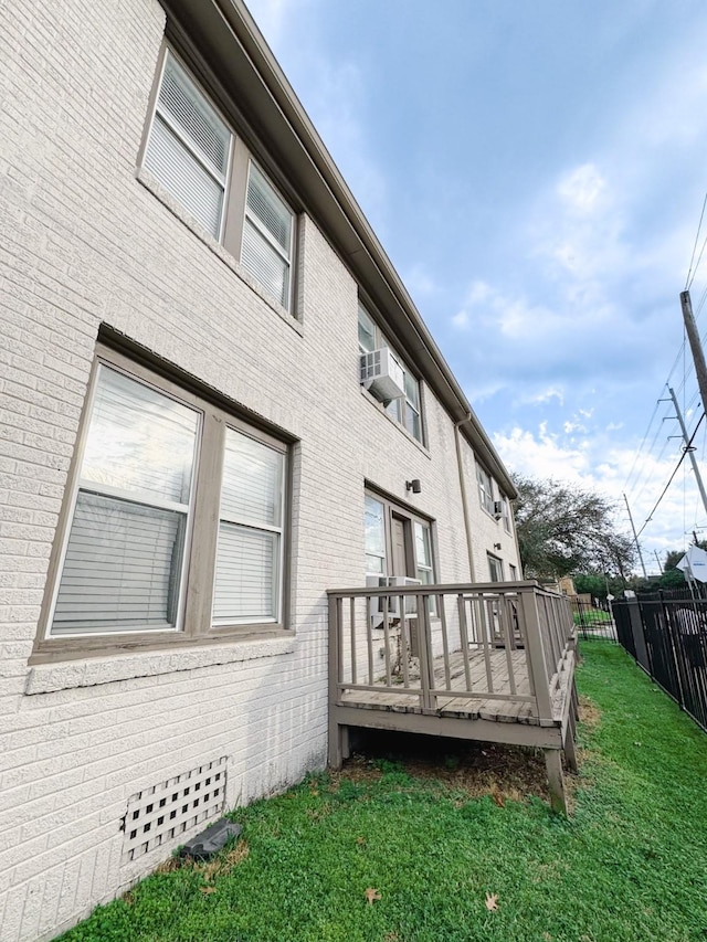 view of property exterior with a yard, a wooden deck, fence, and brick siding