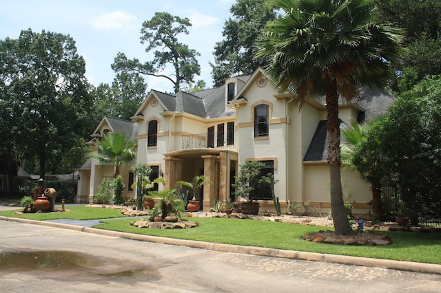 view of front of home featuring a balcony, a front yard, and stucco siding