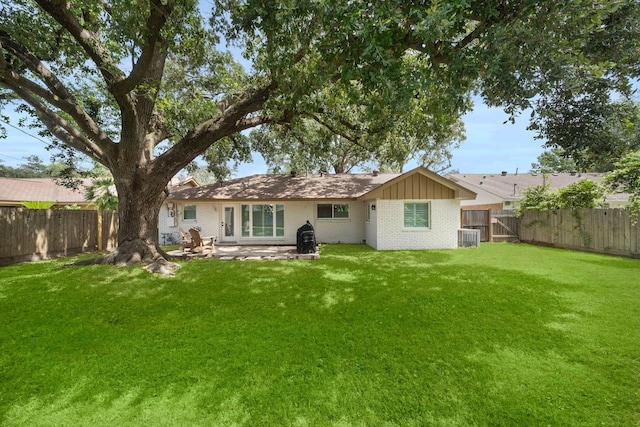 rear view of property featuring brick siding, a lawn, board and batten siding, a patio area, and a fenced backyard