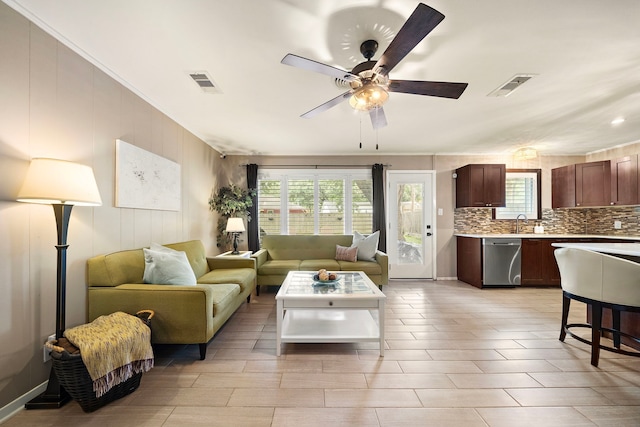 living area with visible vents, a ceiling fan, and ornamental molding