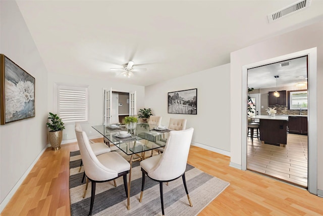 dining room with baseboards, light wood finished floors, visible vents, and a ceiling fan