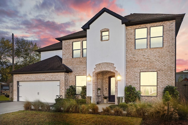 view of front of home with an attached garage, brick siding, a shingled roof, driveway, and stucco siding