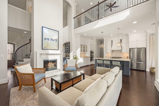 living room featuring a high ceiling, dark wood-style flooring, a fireplace, baseboards, and stairs