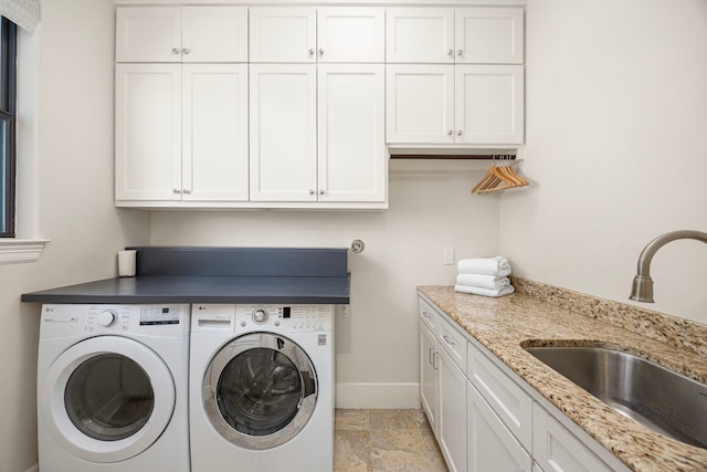 clothes washing area with cabinet space, stone finish flooring, a sink, independent washer and dryer, and baseboards