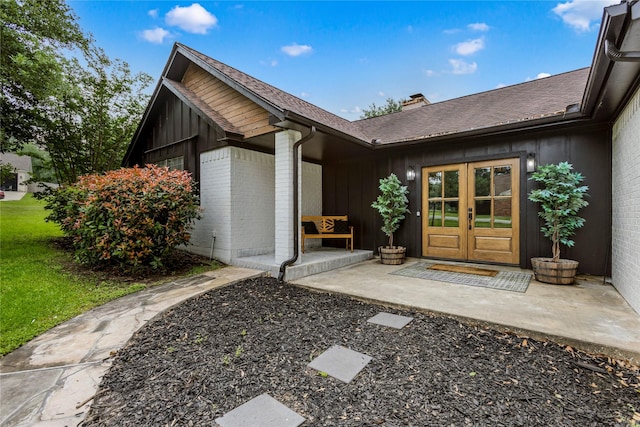 view of exterior entry featuring french doors, brick siding, roof with shingles, and board and batten siding