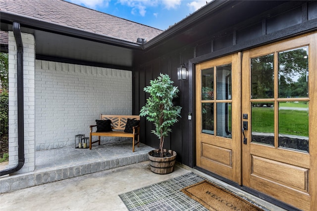 view of exterior entry with french doors, roof with shingles, and brick siding