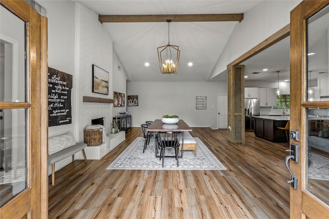 dining room with a brick fireplace, beamed ceiling, and wood finished floors