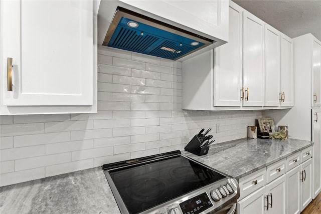 kitchen featuring light stone counters, tasteful backsplash, stainless steel range with electric cooktop, white cabinetry, and wall chimney range hood