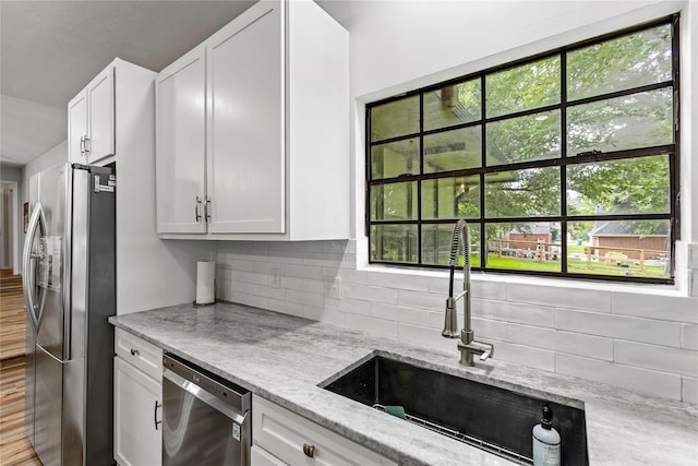 kitchen with light stone counters, a sink, white cabinetry, appliances with stainless steel finishes, and decorative backsplash