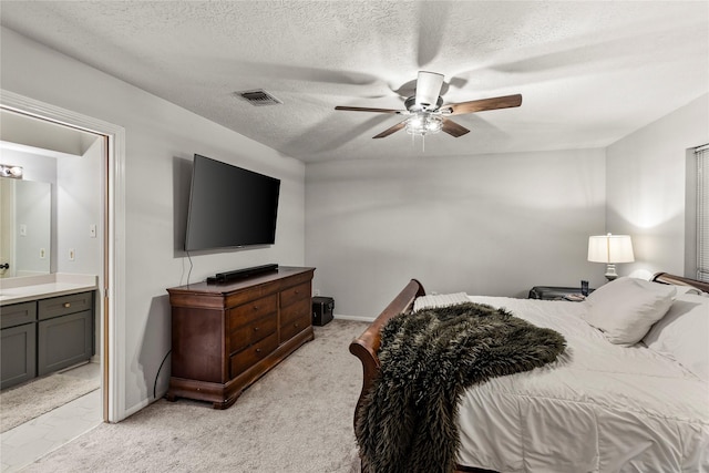 bedroom with light colored carpet, visible vents, connected bathroom, a textured ceiling, and ceiling fan