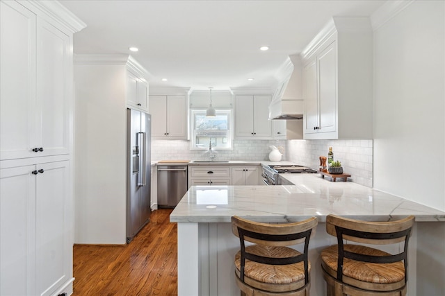 kitchen featuring dark wood-style floors, custom range hood, appliances with stainless steel finishes, ornamental molding, and a peninsula