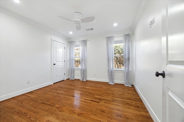 spare room with ceiling fan, wood finished floors, visible vents, baseboards, and ornamental molding