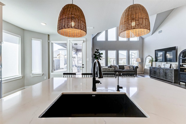 kitchen featuring light stone countertops, visible vents, a sink, a towering ceiling, and pendant lighting