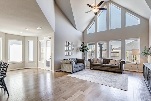 living room featuring a towering ceiling, baseboards, wood finished floors, and a ceiling fan