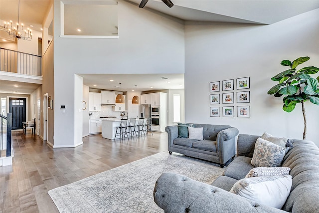 living area with baseboards, light wood-style flooring, recessed lighting, a towering ceiling, and a notable chandelier