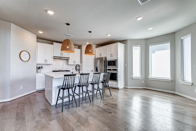 kitchen with a center island with sink, a kitchen bar, decorative backsplash, appliances with stainless steel finishes, and white cabinets