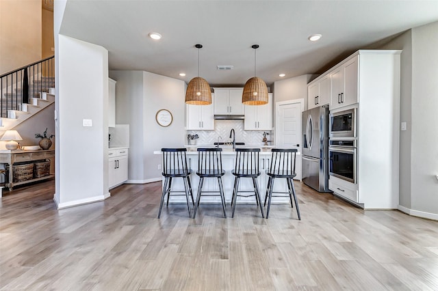 kitchen with stainless steel appliances, backsplash, a kitchen island with sink, and white cabinets