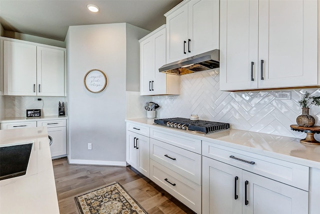 kitchen with light wood-style flooring, under cabinet range hood, stainless steel gas stovetop, white cabinets, and light countertops