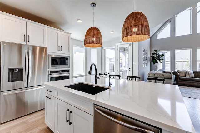 kitchen featuring pendant lighting, light wood-style flooring, a center island with sink, a sink, and stainless steel appliances