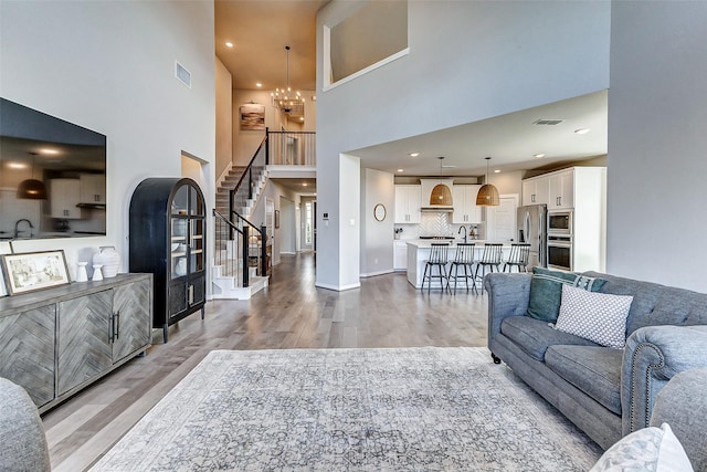 living area featuring stairway, visible vents, a chandelier, and light wood-type flooring