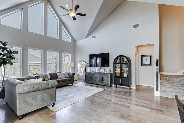 living room with light wood-type flooring, visible vents, a ceiling fan, and stairs