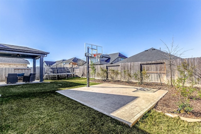 view of basketball court featuring a lawn, a fenced backyard, and a trampoline