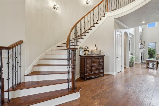 stairway with crown molding, a fireplace, a towering ceiling, baseboards, and hardwood / wood-style flooring