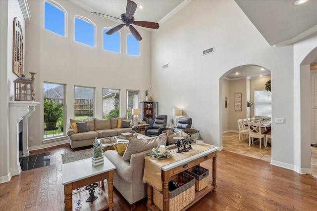 living area featuring arched walkways, ornamental molding, wood finished floors, and a ceiling fan