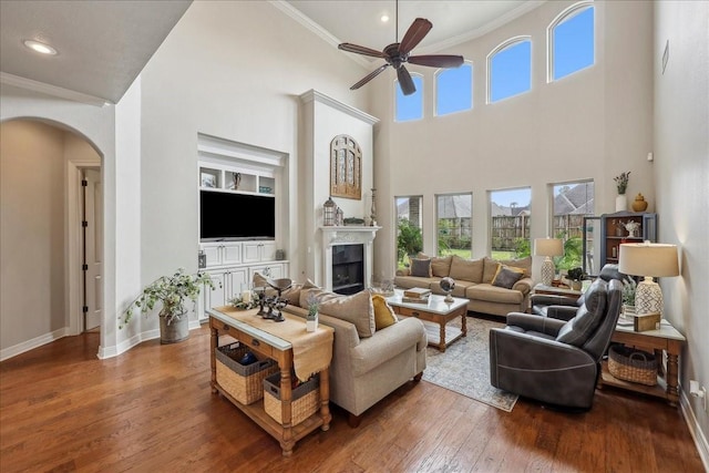 living room featuring arched walkways, a fireplace, crown molding, wood-type flooring, and baseboards