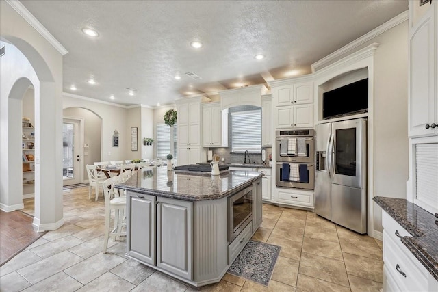 kitchen with a sink, appliances with stainless steel finishes, dark stone countertops, and a kitchen bar