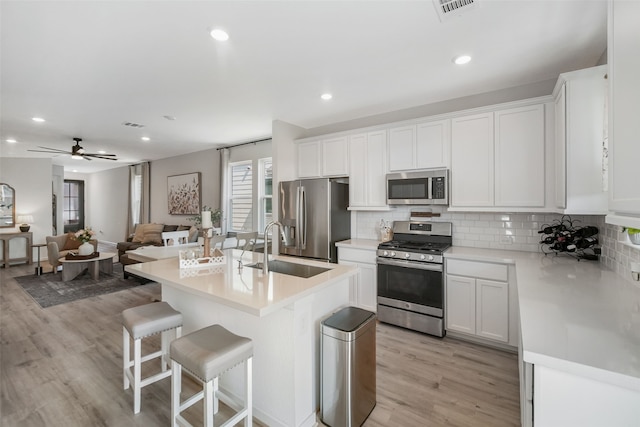 kitchen featuring tasteful backsplash, appliances with stainless steel finishes, white cabinetry, a sink, and a kitchen bar