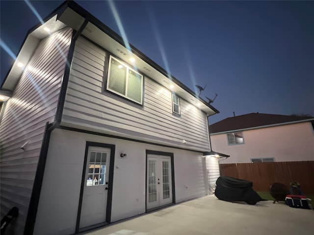 back of house at night featuring french doors, a patio area, and fence