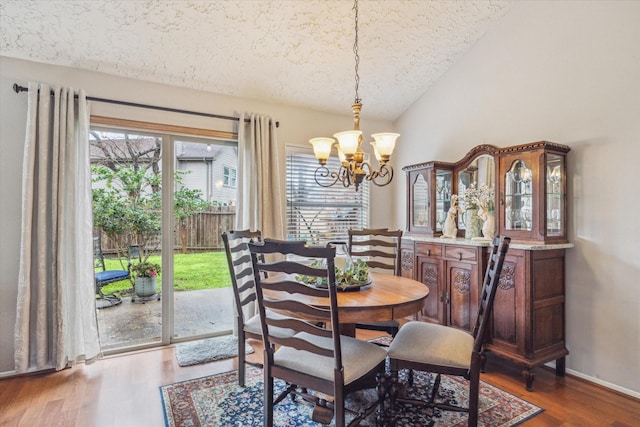 dining room featuring baseboards, lofted ceiling, wood finished floors, an inviting chandelier, and a textured ceiling