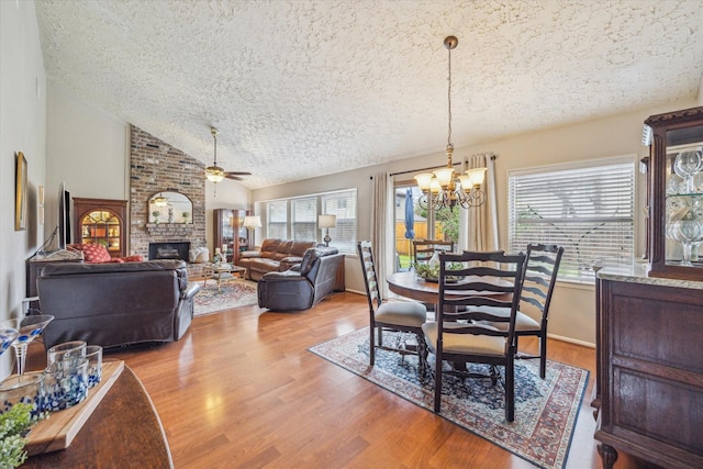 dining area featuring lofted ceiling, a textured ceiling, ceiling fan with notable chandelier, a fireplace, and wood finished floors