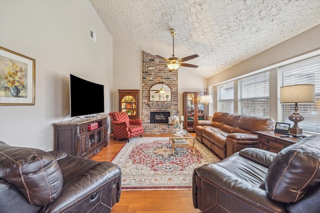 living area featuring ceiling fan, light wood-style flooring, a fireplace, and vaulted ceiling