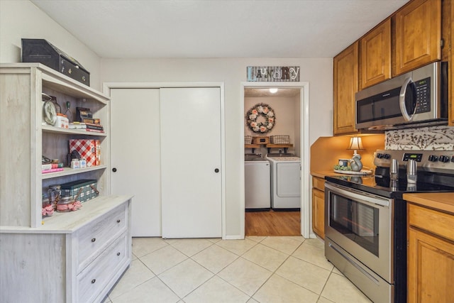 kitchen with light tile patterned floors, appliances with stainless steel finishes, independent washer and dryer, open shelves, and brown cabinetry