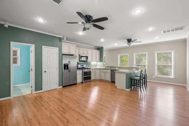 kitchen with stainless steel appliances, a breakfast bar, a peninsula, visible vents, and ornamental molding