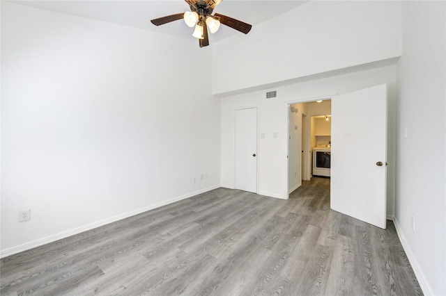 unfurnished bedroom featuring visible vents, a towering ceiling, a ceiling fan, wood finished floors, and baseboards