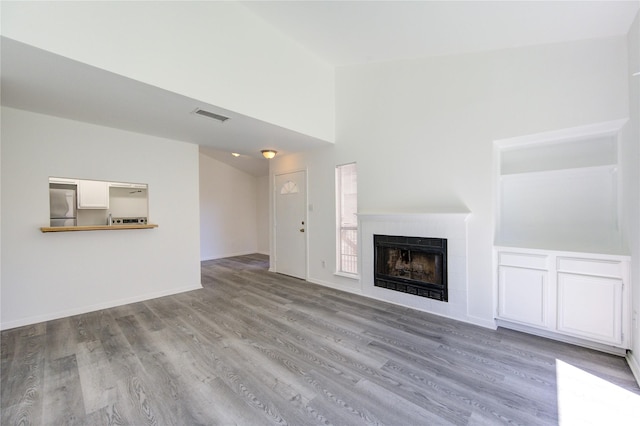 unfurnished living room with lofted ceiling, visible vents, wood finished floors, a tile fireplace, and baseboards